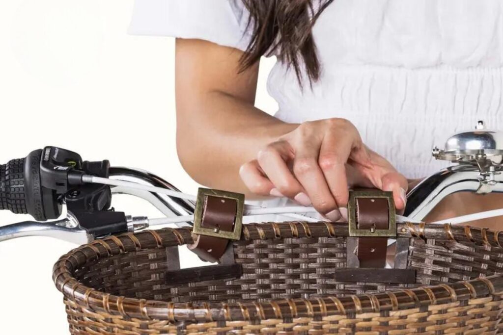 A woman attaching a wicker basket to a bicycle.