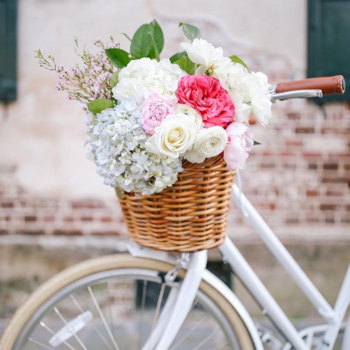 Flowers arranged in a wicker bike baskets attached to a white bicycle